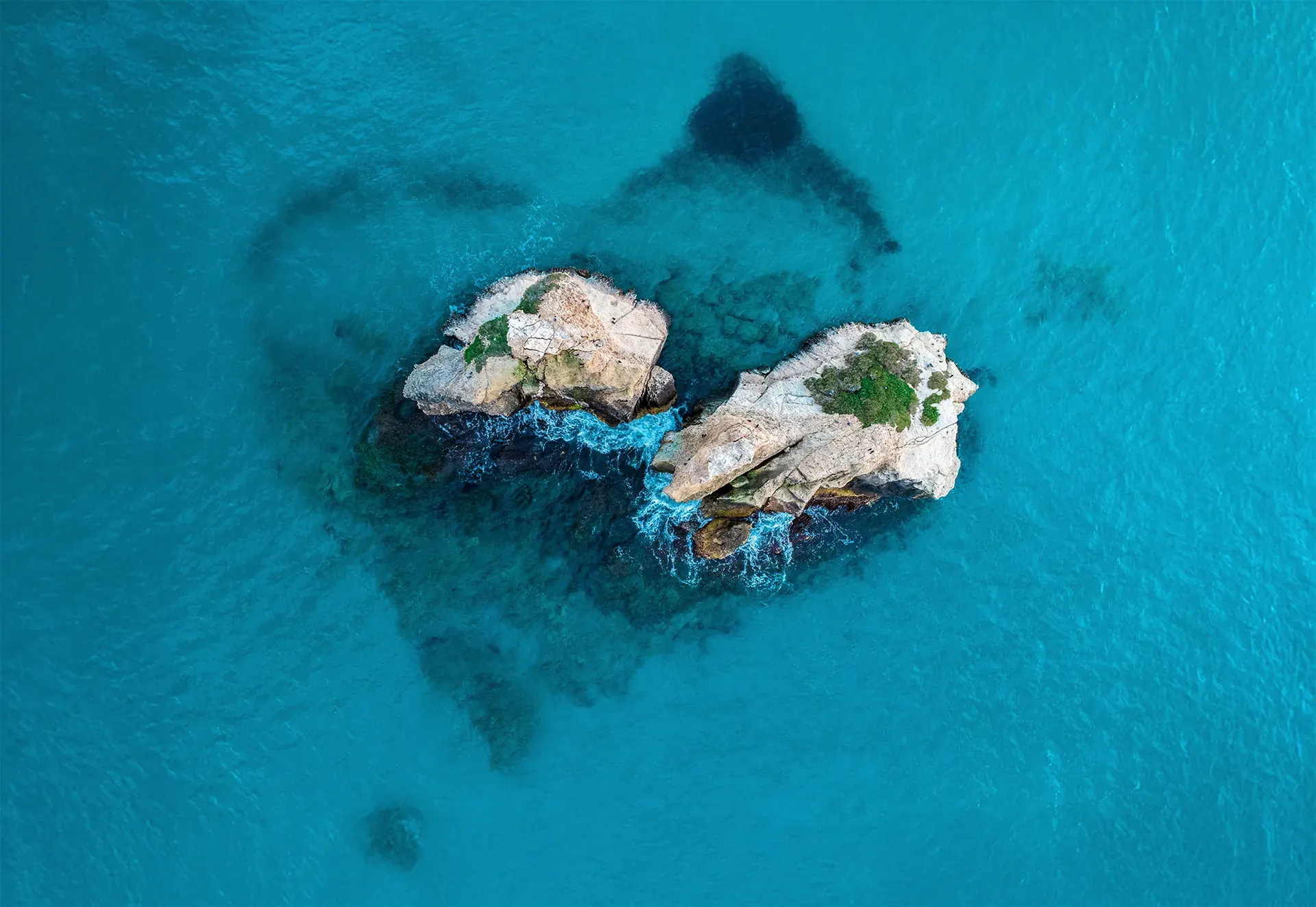 Zwei Felseninseln im türkisen Meer, deren Schattenwurf eine Herzform bildet, Drohnenaufnahme